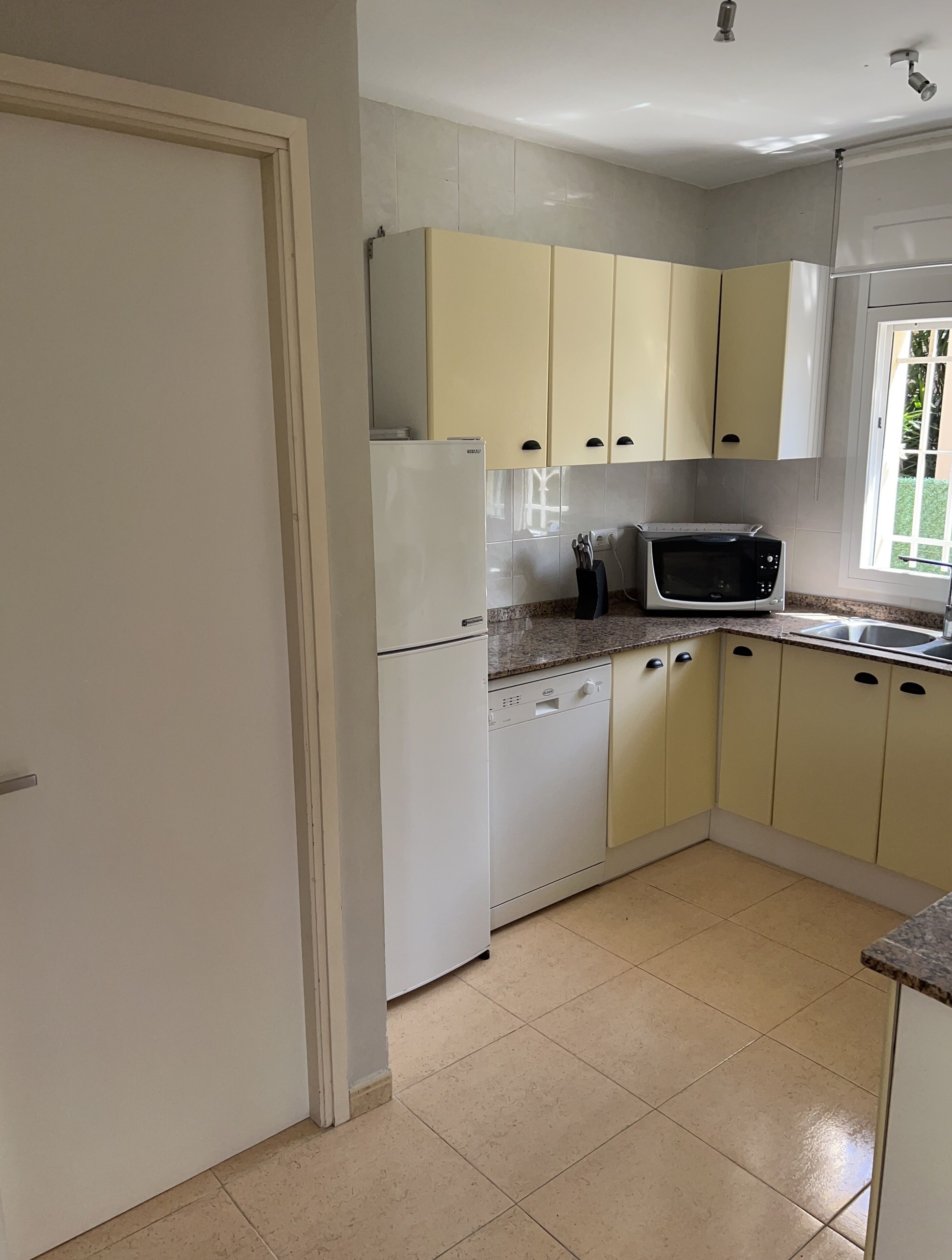 A kitchen with white and yellow cabinets, a white refrigerator, a microwave, and a dishwasher.
