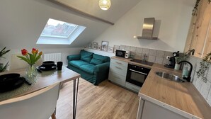A modern kitchen with a skylight, a dining area with a table and chairs, and a teal sofa. - Studio Les Tulipes (Calais)