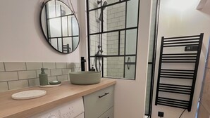 A compact laundry area with a washing machine, a sink with a bowl, a mirror, and a towel rack. - Studio Les Tulipes (Calais)