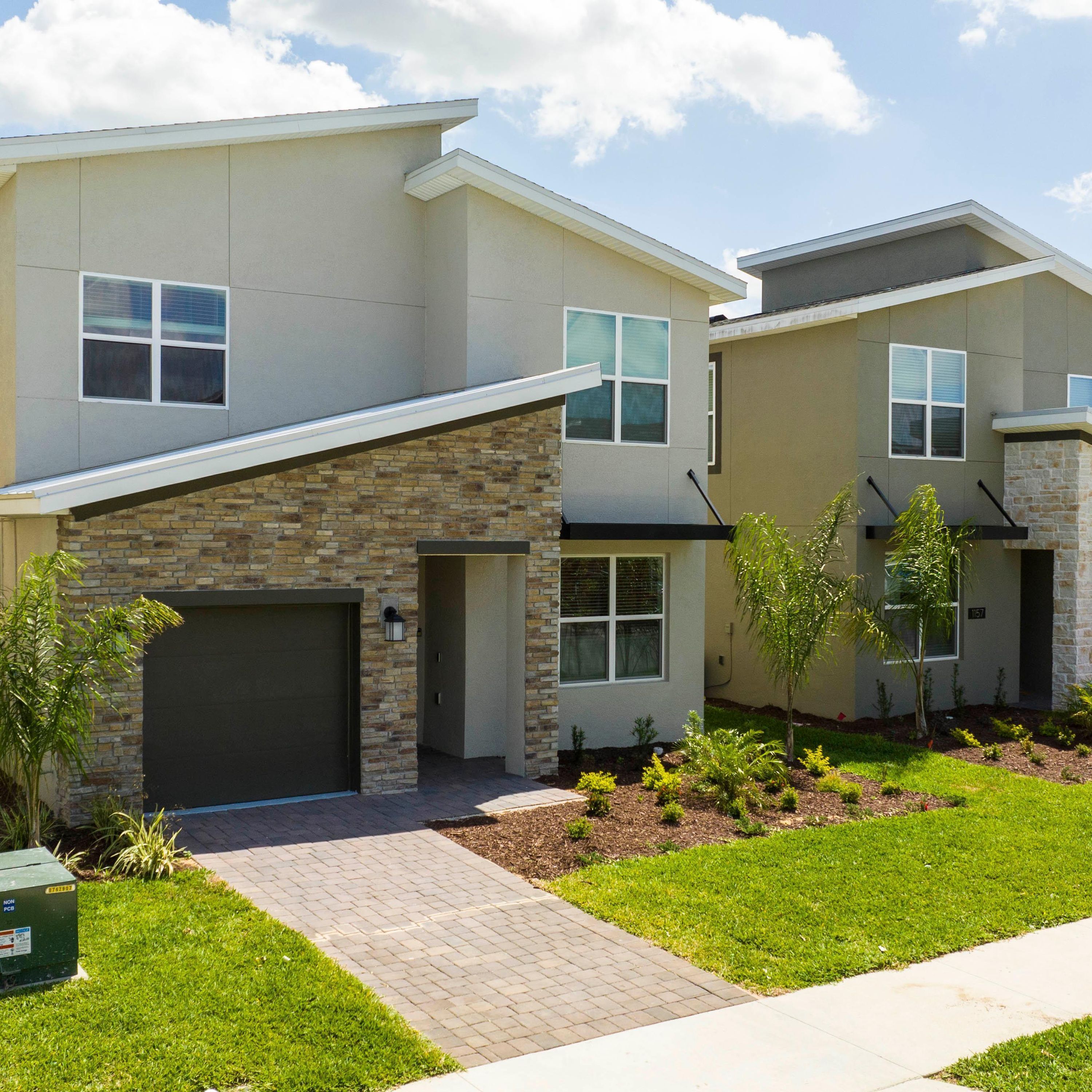 A modern two-story residential building with a stone facade, a garage, and a well-maintained lawn.