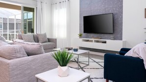 Ein modernes Wohnzimmer mit einem grauen Sofa, einem blauen Sessel, einem weißen Couchtisch und einem Flachbildfernseher, der an einer grauen, strukturierten Wand montiert ist.