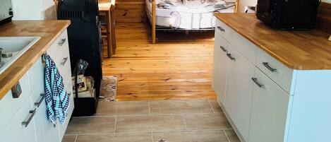 Una cocina funcional con una mesa de madera, una cama con ropa de cama floral y un microondas en la encimera.
