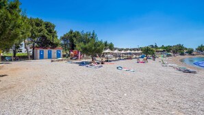 A beach with a small building, beach umbrellas, and people relaxing. - 6BD Villa for 12 with Heated Pool, Jacuzzi, First Row to the Sea (Punat)