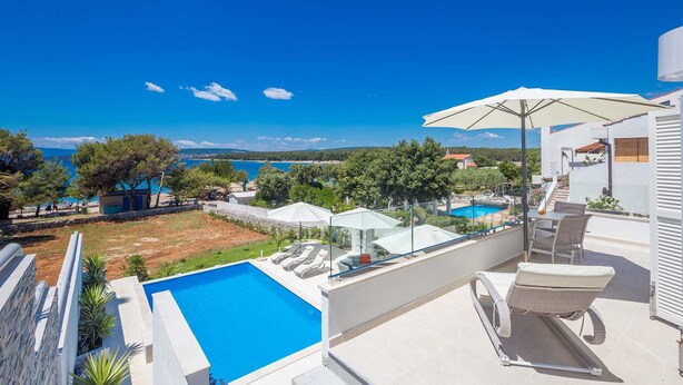 A poolside area with a clear view of the sea, a white building, and a covered seating area. - 6BD Villa for 12 with Heated Pool, Jacuzzi, First Row to the Sea (Punat)