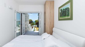 A bedroom with a bed, a wooden wardrobe, a framed painting, and a view of a pool and trees. - 6BD Villa for 12 with Heated Pool, Jacuzzi, First Row to the Sea (Punat)