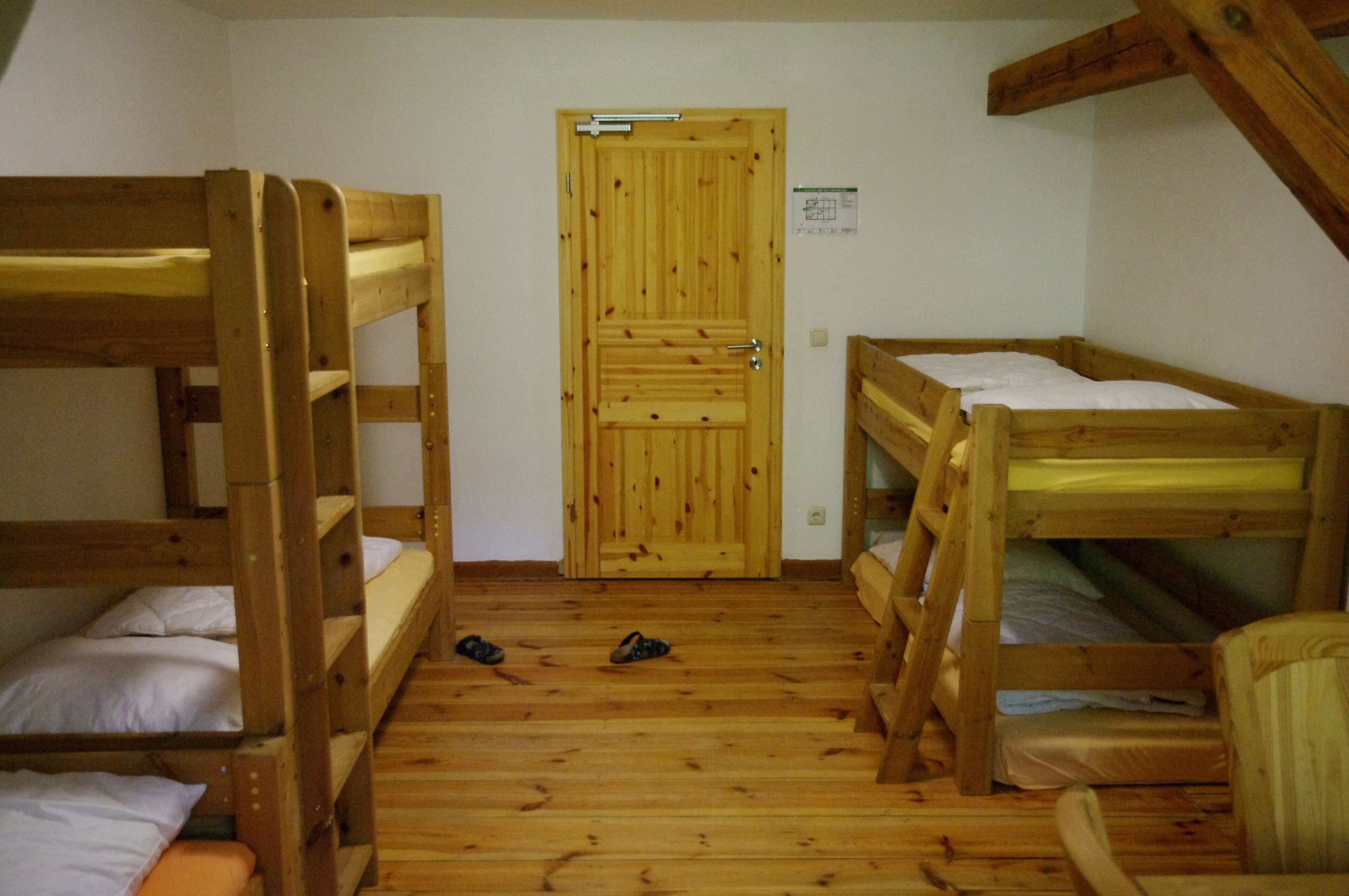 A room with three bunk beds, a wooden door, and a pair of shoes on the floor.