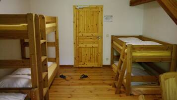 A room with three bunk beds, a wooden door, and a pair of shoes on the floor.