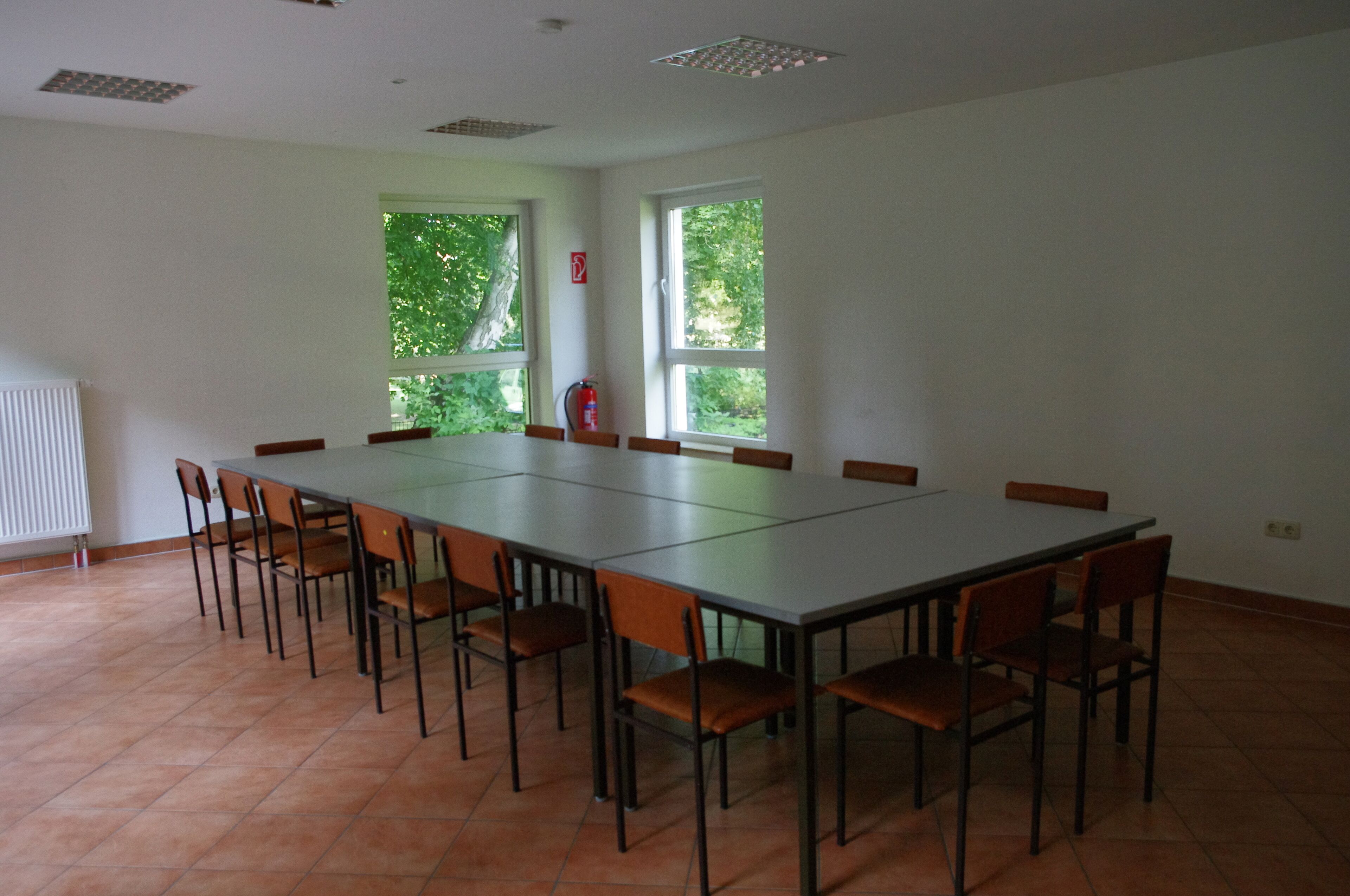 A conference room with a long table and chairs, large windows with a view of greenery, and a fire extinguisher on the wall.