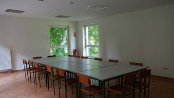 A conference room with a long table and chairs, large windows with a view of greenery, and a fire extinguisher on the wall.