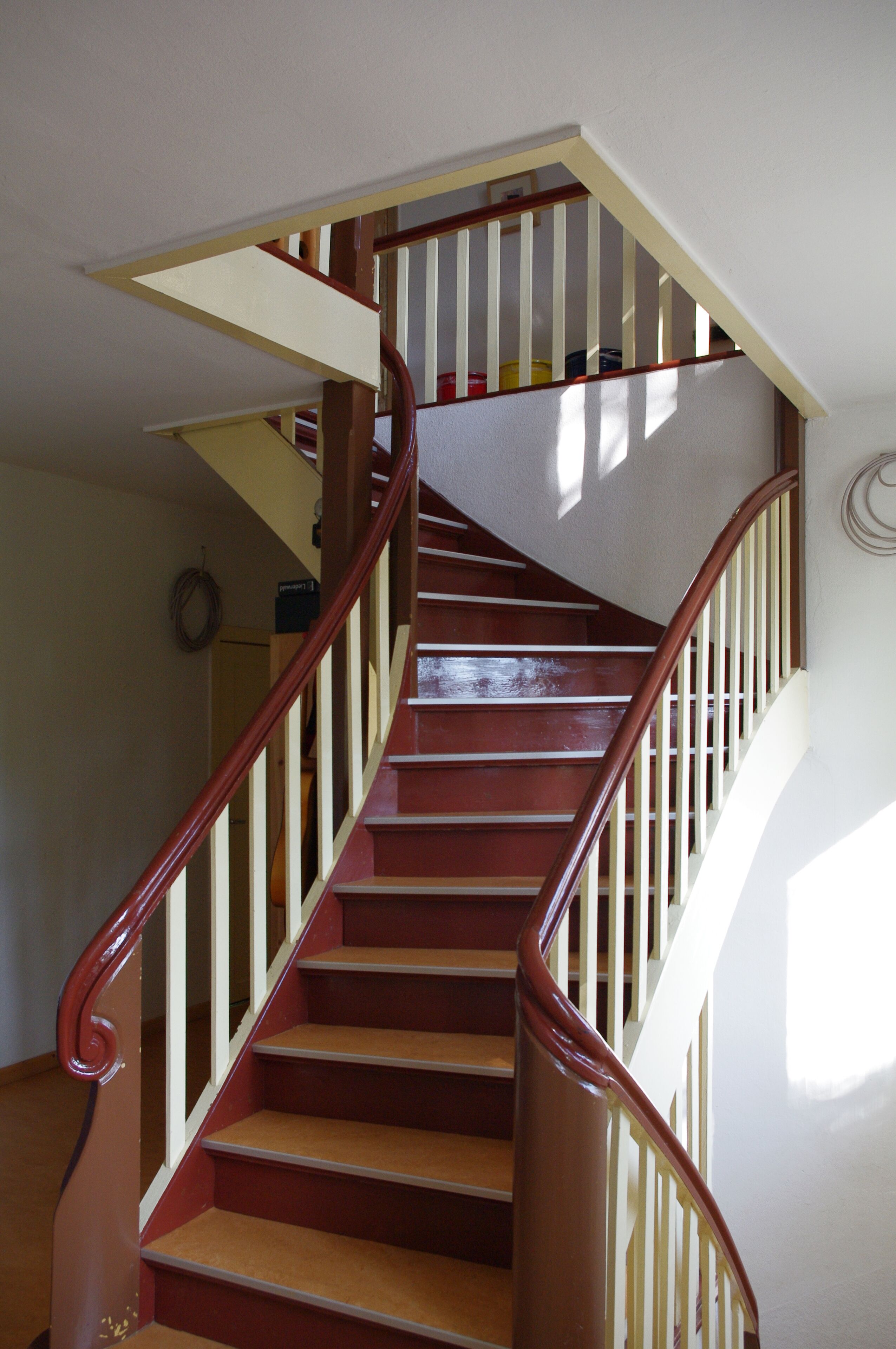 Un escalier en bois avec des rampes blanches et une main courante rouge.