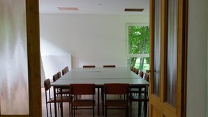 Un salón de conferencias con una larga mesa y sillas, una ventana que ofrece vistas a árboles, y una puerta con letreros de salida de emergencia.