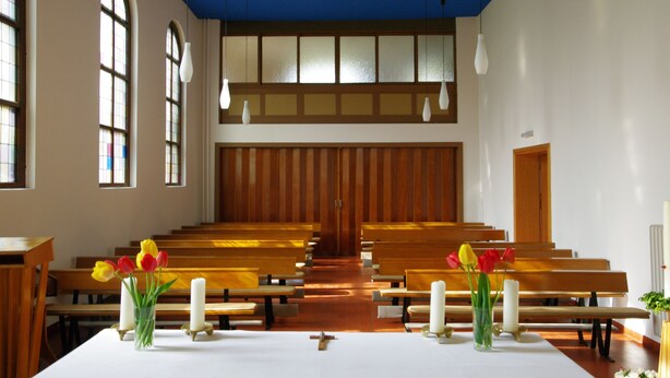 Interior de iglesia con bancos de madera, altar blanco y una cruz.