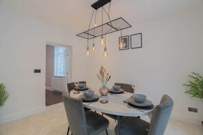 A dining area with a round table, chairs, a hanging light fixture, and a vase with dried plants.