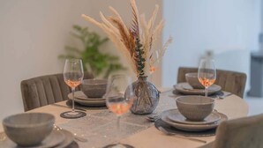 A dining table set with plates, bowls, and glasses, and a vase with dried plants.
