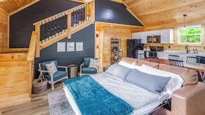 A cozy cabin interior with a bed, seating area, kitchen, and a staircase. - Riverfront Cabin~Firepit~Private Boat Ramp w/ river access~Dog-Friendly! (Jamestown)