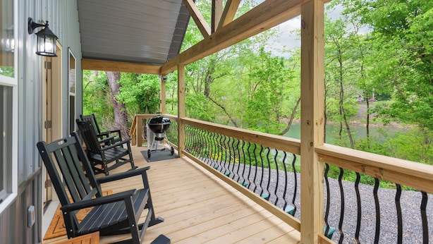 A covered deck with wooden chairs and a grill, overlooking a forested area and a body of water. - Riverfront Cabin~Firepit~Private Boat Ramp w/ river access~Dog-Friendly! (Jamestown)