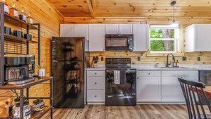 A modern kitchen with white cabinets, stainless steel appliances, and wooden flooring. - Riverfront Cabin~Firepit~Private Boat Ramp w/ river access~Dog-Friendly! (Jamestown)
