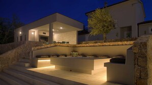 A modern outdoor seating area with stone steps leading up to it, a stone wall, and a tree.