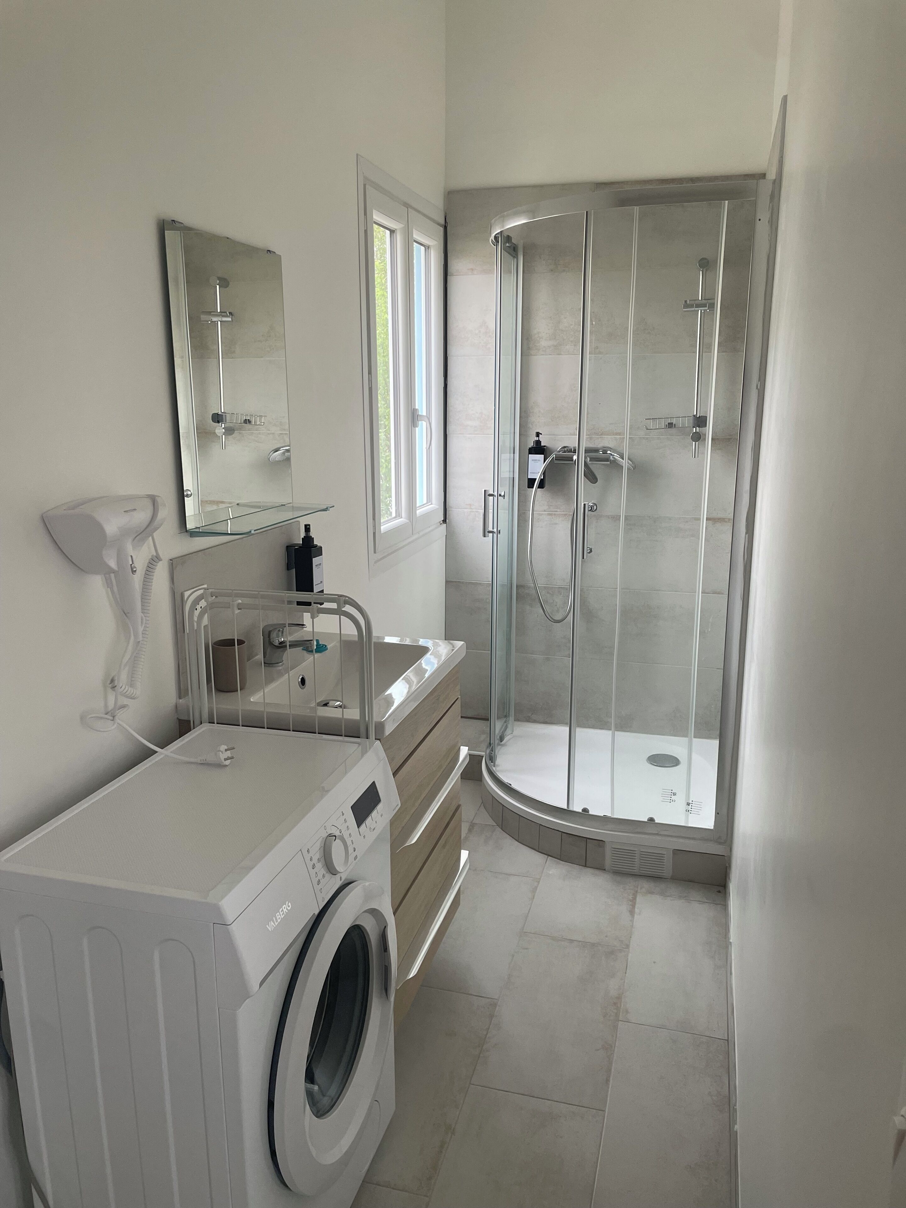 A modern bathroom with a built-in washing machine, a glass shower enclosure, and a vanity with a mirror.