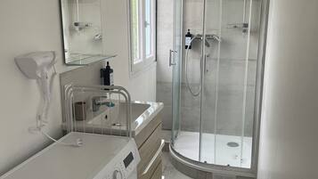 A modern bathroom with a built-in washing machine, a glass shower enclosure, and a vanity with a mirror.
