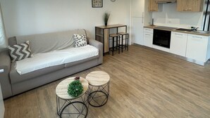 Una sala de estar moderna con un sofá gris, dos mesas redondas y una planta pequeña.
