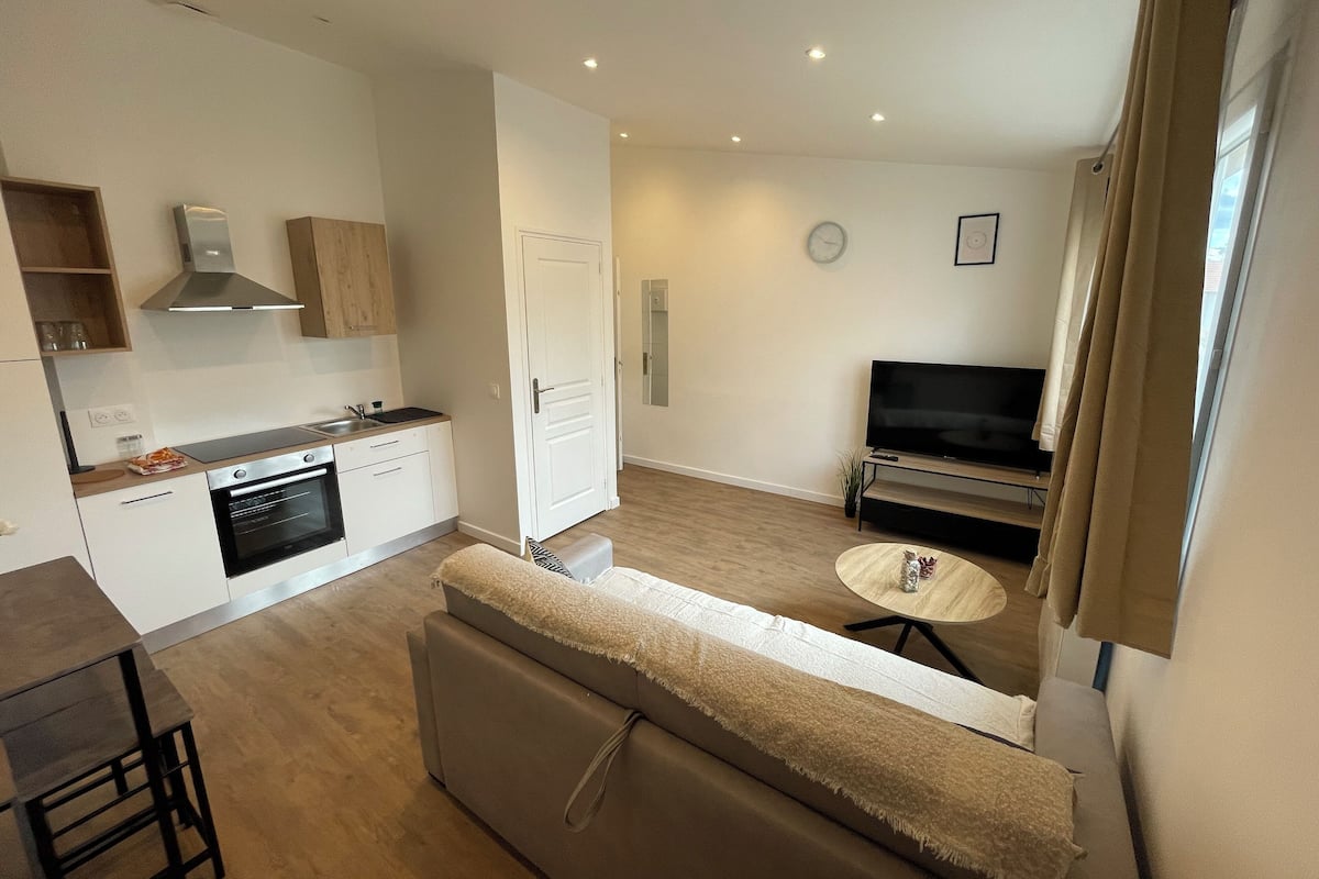 Um apartamento moderno com cozinha compacta, sala de estar com sofá e TV, e área de jantar com mesa e cadeiras.