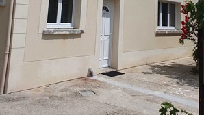 Un edificio de dos pisos con fachada color crema, dos ventanas en la planta baja y una puerta con un pequeño ventanal encima.
