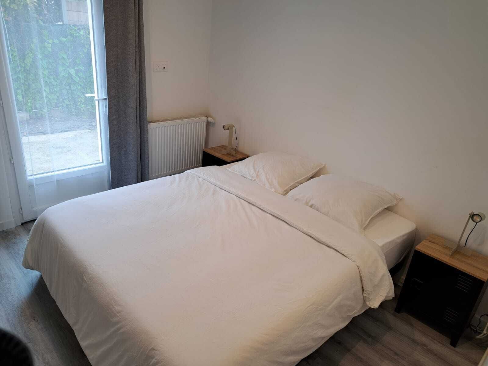 A bedroom with a bed, a nightstand, a lamp, and a window with curtains.