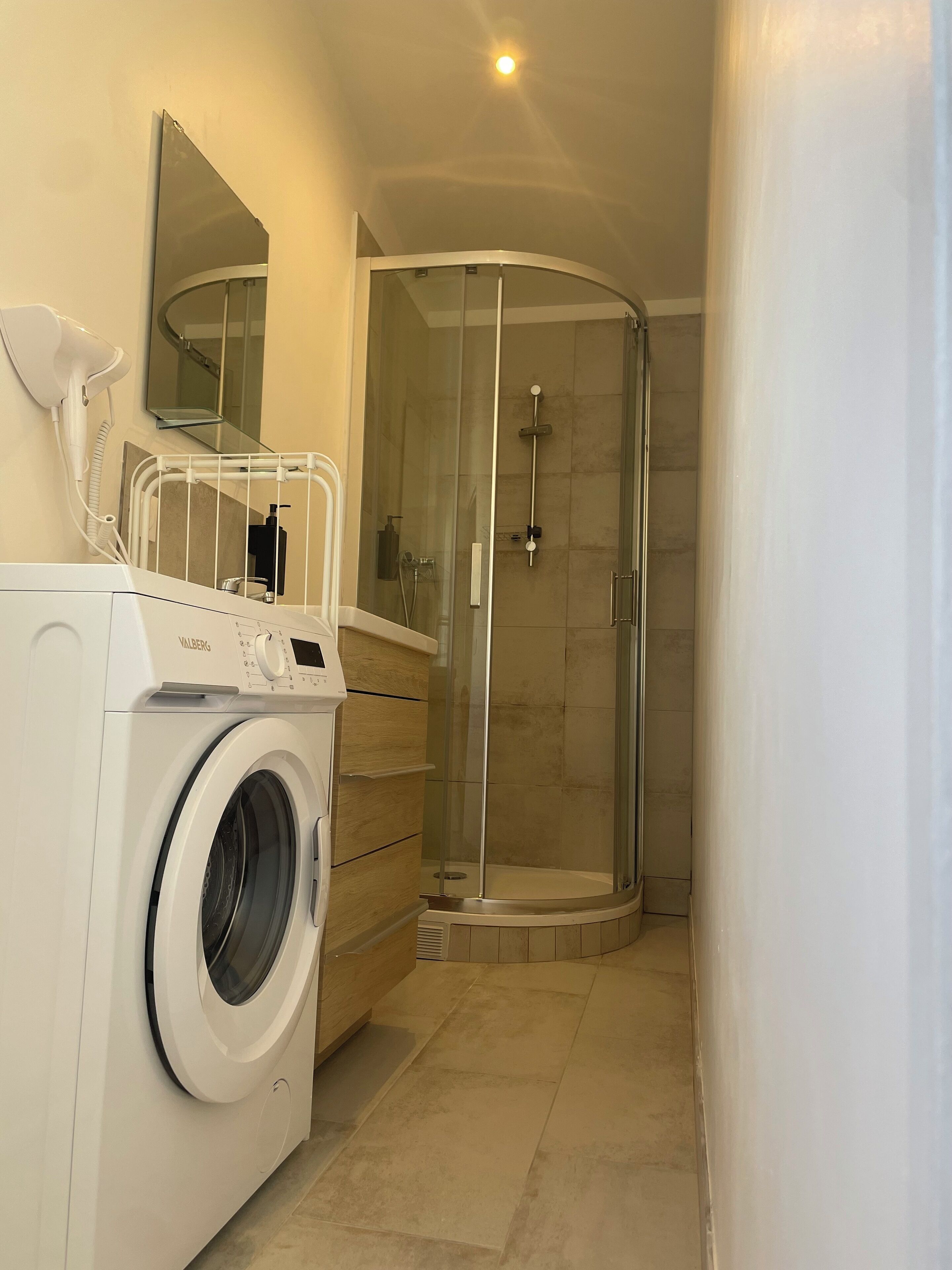 Une petite salle de bain équipée d’un lave-linge, d’une douche à parois de verre et d’un miroir au-dessus du lavabo.