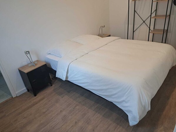 A bedroom with a bed, a nightstand, and a wall-mounted shelf.