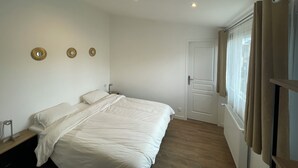 Un dormitorio con cama, mesita de noche, puerta y ventana con cortinas.