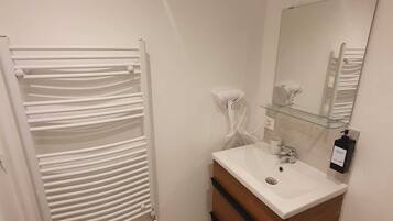 Un baño con un radiador blanco, un lavabo con un espejo encima y un bolso amarillo en el suelo.