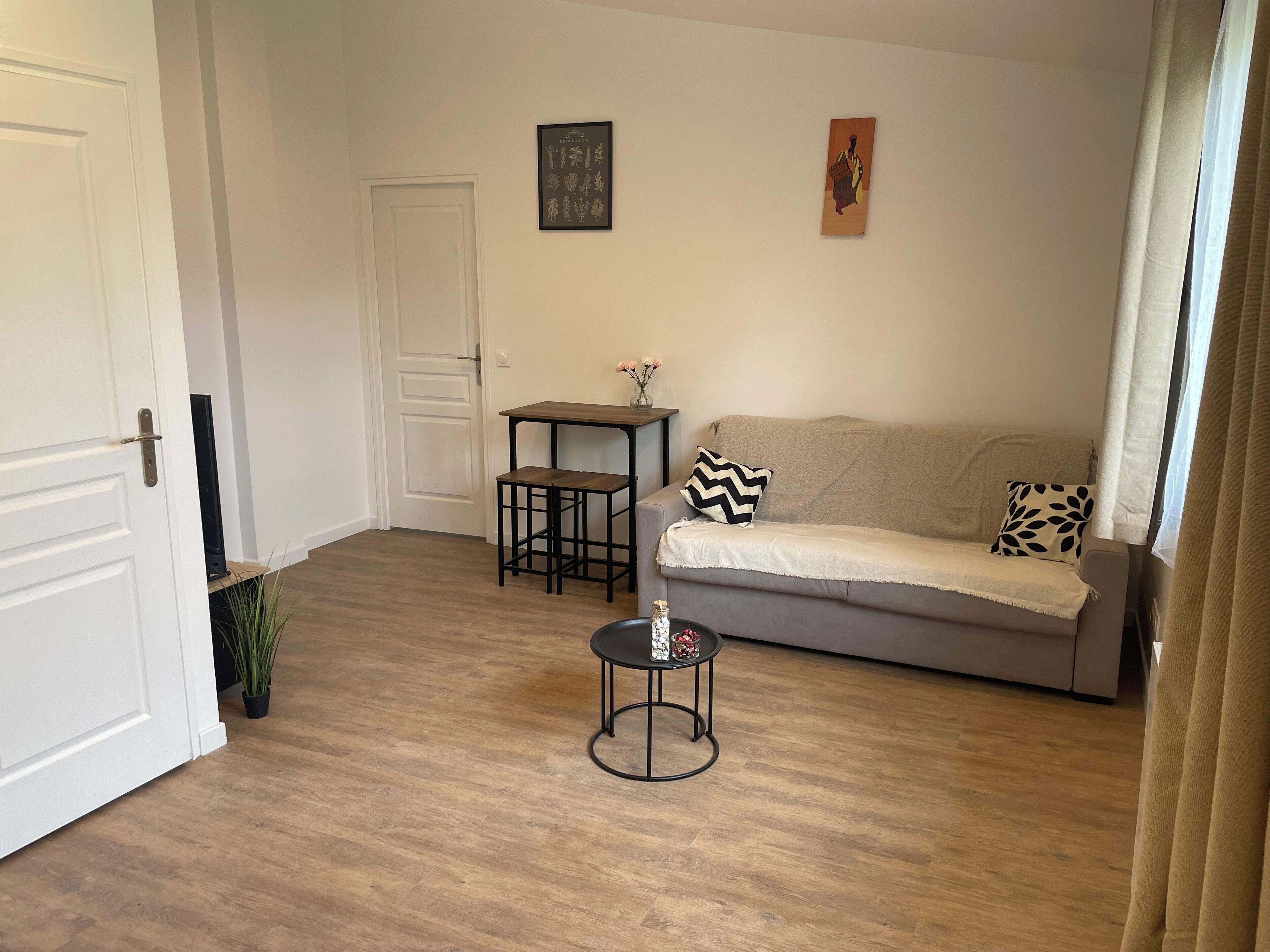 A living room with a grey sofa, a small black table, a white door, and a framed picture on the wall.