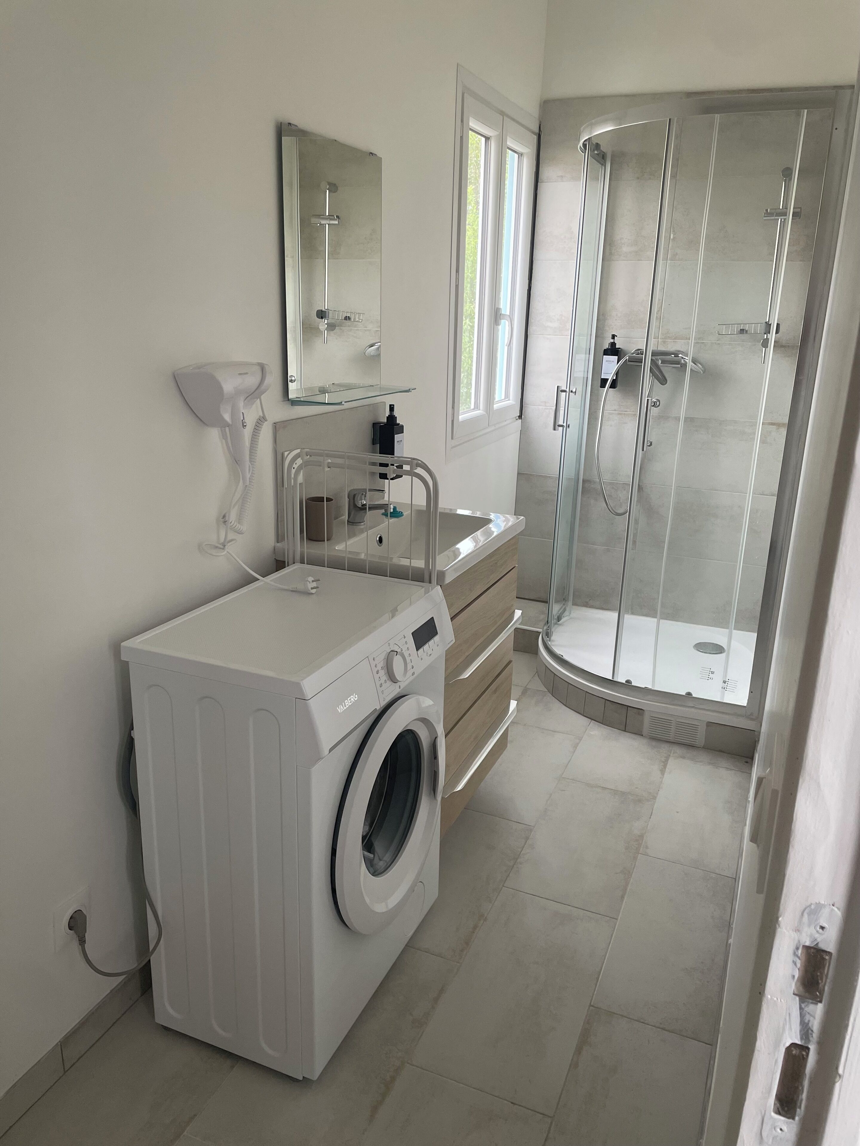 Une salle de bain moderne équipée d’un lave-linge intégré, d’une douche en verre et d’un meuble-lavabo avec miroir.