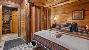 Una stanza in legno con un letto, un comodino, una lampada e un quadro appeso al muro.