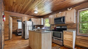 Cucina di una baita in legno con isola centrale, forno a microonde integrato, elettrodomestici in acciaio inossidabile e un'ampia finestra con vista sull'esterno.