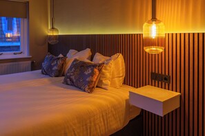 Una cama bien hecha con un cojín blanco y azul con estampado floral, una mesita de noche y una lámpara de pared.