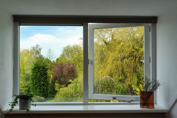 A window with a view of a garden, a potted plant on the windowsill, and a wooden frame. - B&B Dijkhuis (Vrouwenpolder)