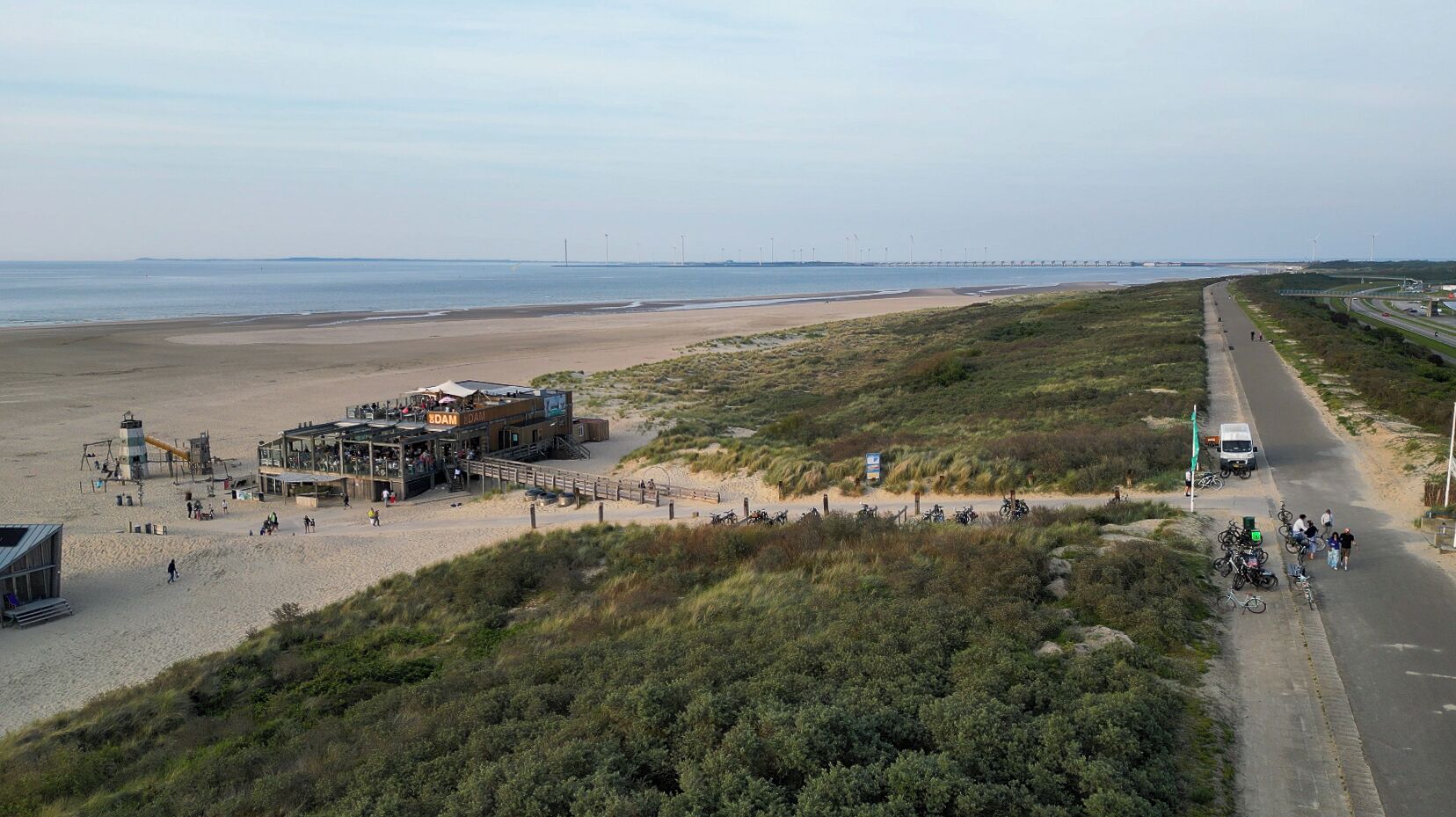 Eine Lage am Strand mit Rettungsschwimmerstation, einer parallel zum Strand verlaufenden Straße und abgestellten Fahrrädern am Straßenrand.