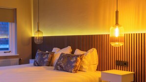 Camera da letto moderna con un letto grande, due lampade a sospensione, un comodino e una finestra con tende.