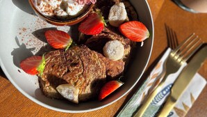 Un piattino con fragole, un fiore e una piccola ciotola di panna montata su un tavolo di legno.