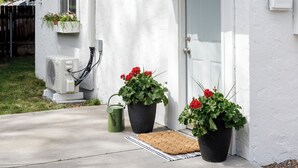 A white house with a black roof, a front door, and a small porch. There are two potted plants with red flowers on the porch. - Charming Cottage on the Boise Bench. Minutes from downtown, BSU & the airport. (Boise)