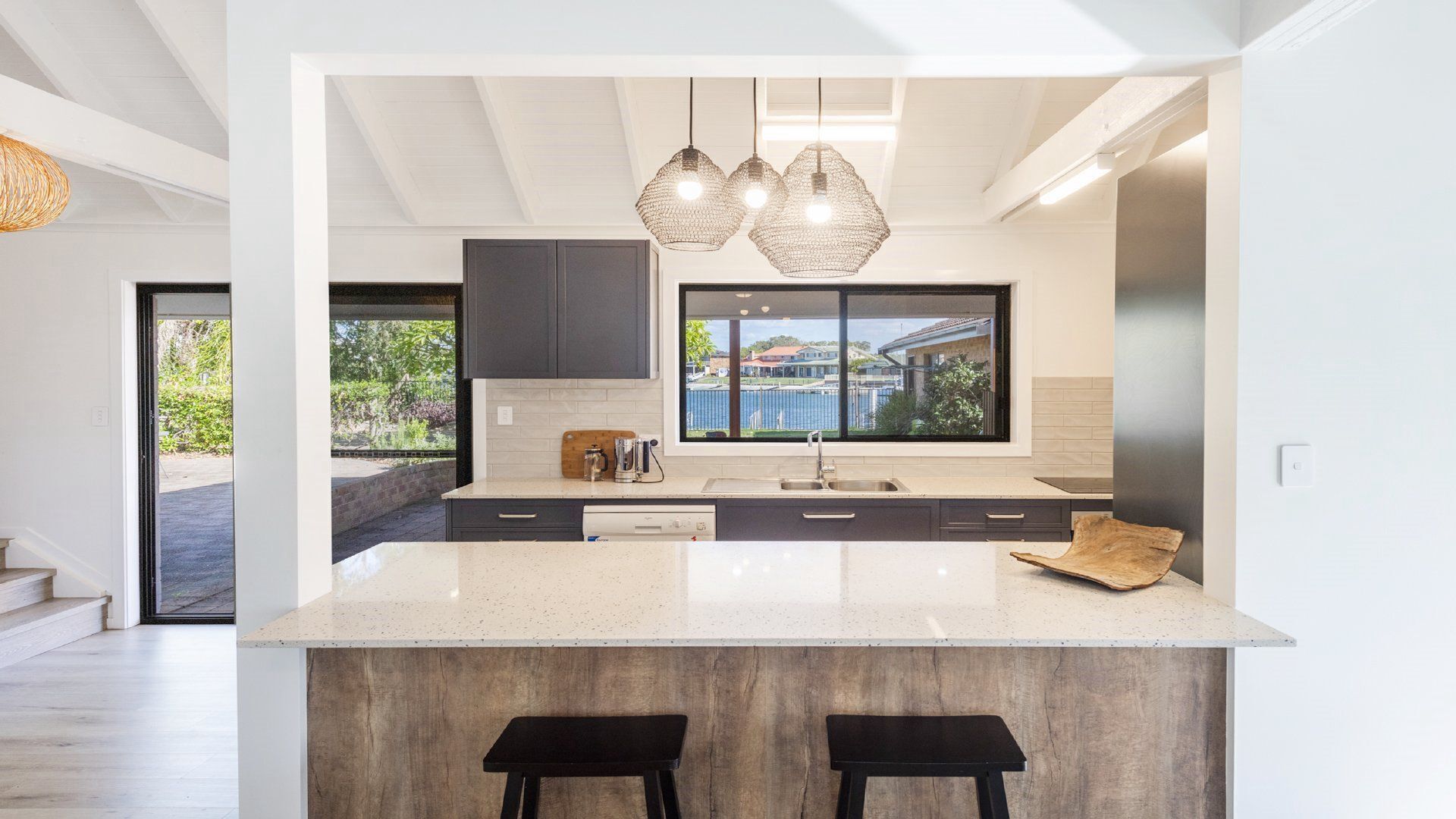 A modern kitchen with a large island, dark cabinetry, and a view of the outdoors.