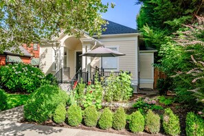 A two-story house with a front porch, a covered patio, and a well-maintained garden with various plants and shrubs. - OSU Campus Cottage on SW 7th Street - Breakfast Included (Corvallis)