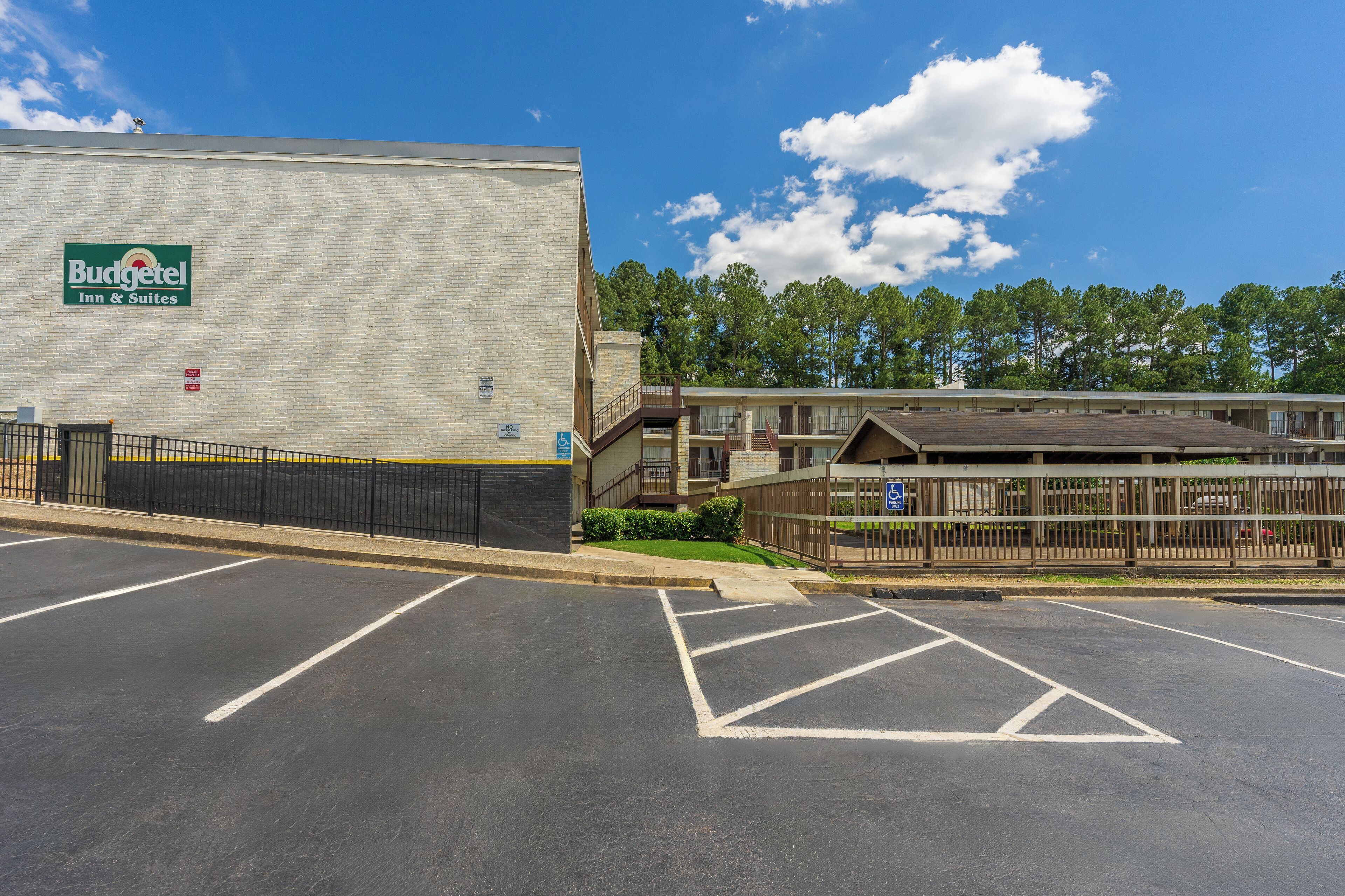 A parking lot with marked spaces, a Budgetel Inn & Suites building, and a fenced area with a building in the background.