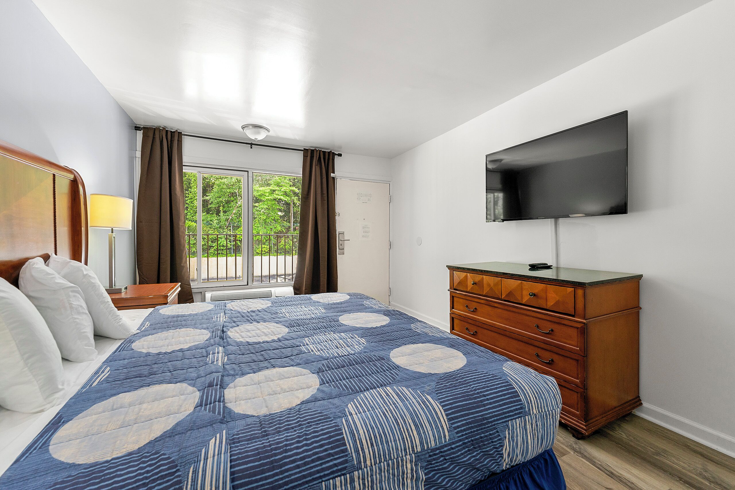 Ein Schlafzimmer mit Bett, Schminktisch, Fernseher und einem Fenster mit Vorhängen.