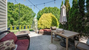 Patio esterno con tavolo di legno e sedie in vimini, immerso nel verde e illuminato da luci a catena.