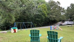 A grassy area with a swing set, a small playhouse, and two green chairs. - RV Site #42 pull through - Big Rig Friendly 65ftx28ft (Hardin)