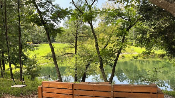 A wooden bench with a metal frame, positioned in a natural setting with a pond and trees in the background. - RV Site #42 pull through - Big Rig Friendly 65ftx28ft (Hardin)