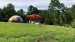 A camping site with a tent and a red canopy, surrounded by trees and grass. - RV Site #38 Pull Through (Hardin)